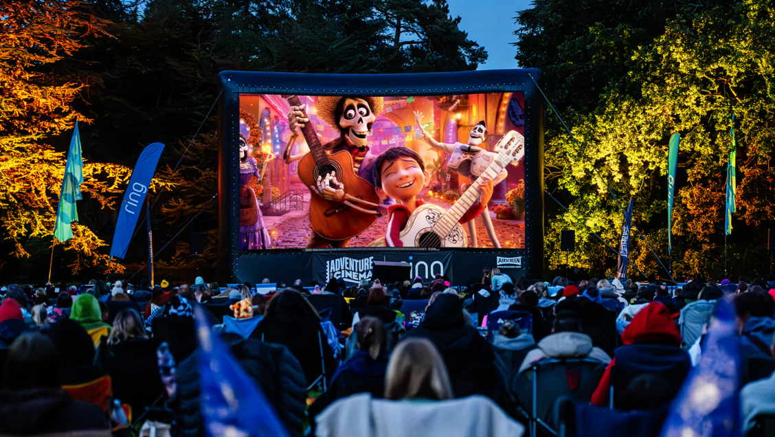 Screenshot of the movie Coco - a young boy playing the guitar with a skeleton. On a big screen